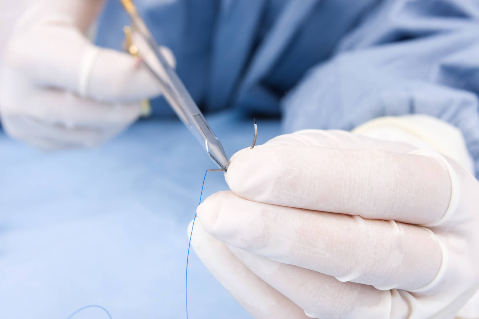 Veterinarian in scrubs and white surgical gloves holding Securos suture
